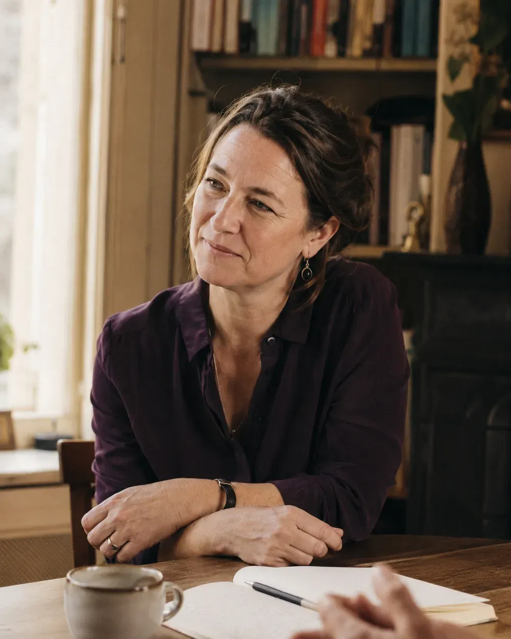 De coach aan haar werktafel bij het raam, luisterend